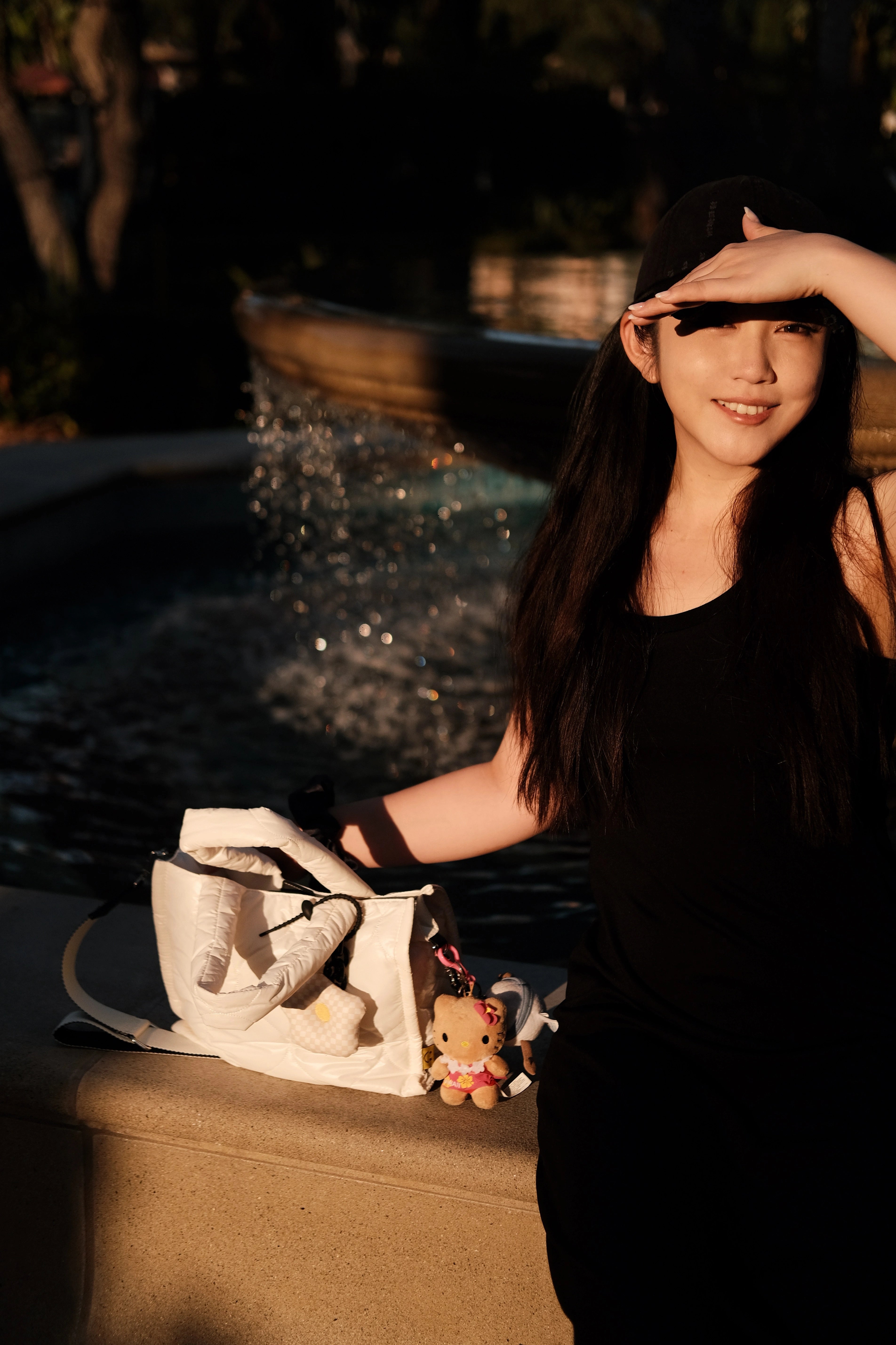 Model holding a white puffer tote bag while sitting by a fountain