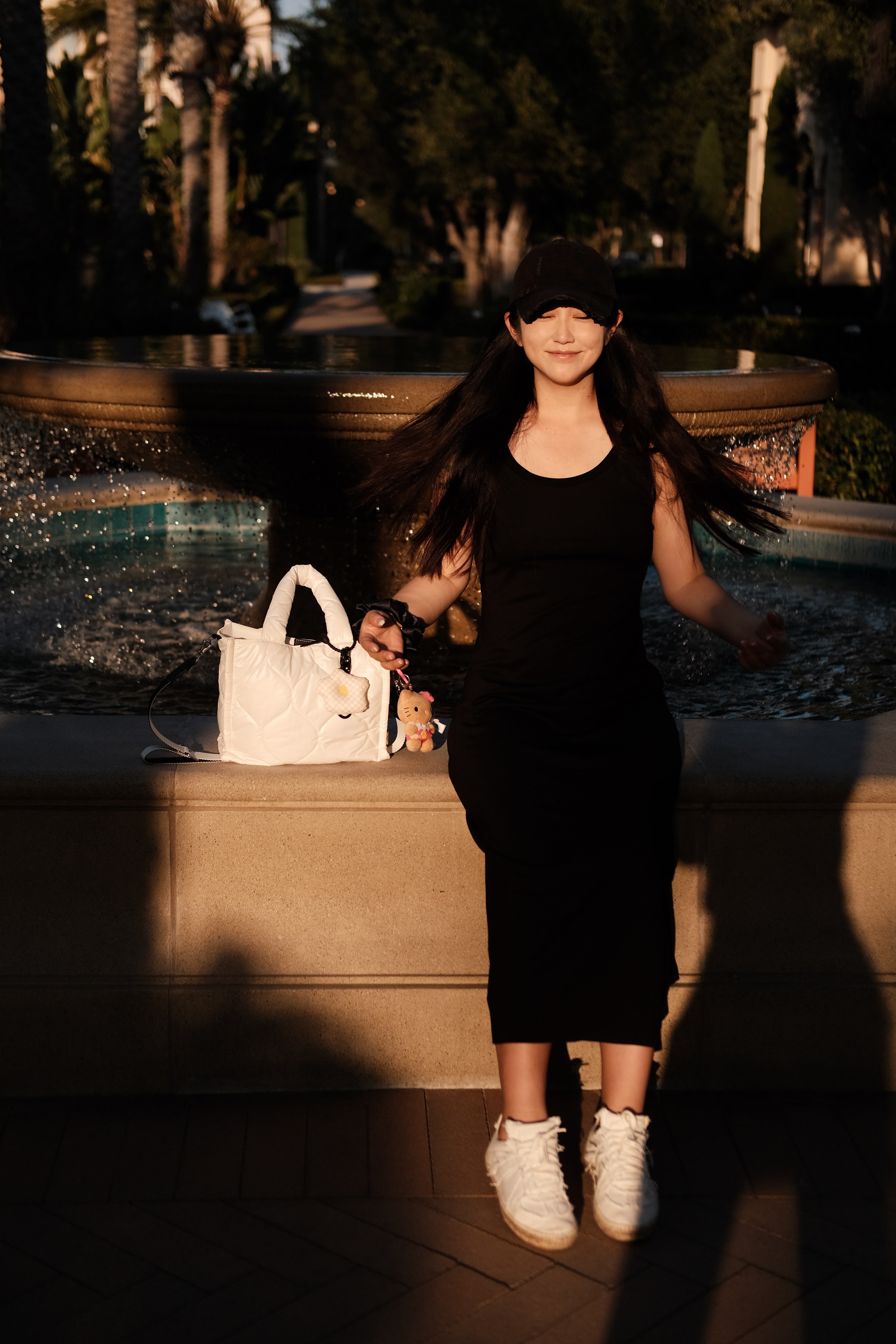 Model holding a white puffer tote bag while sitting by a fountain