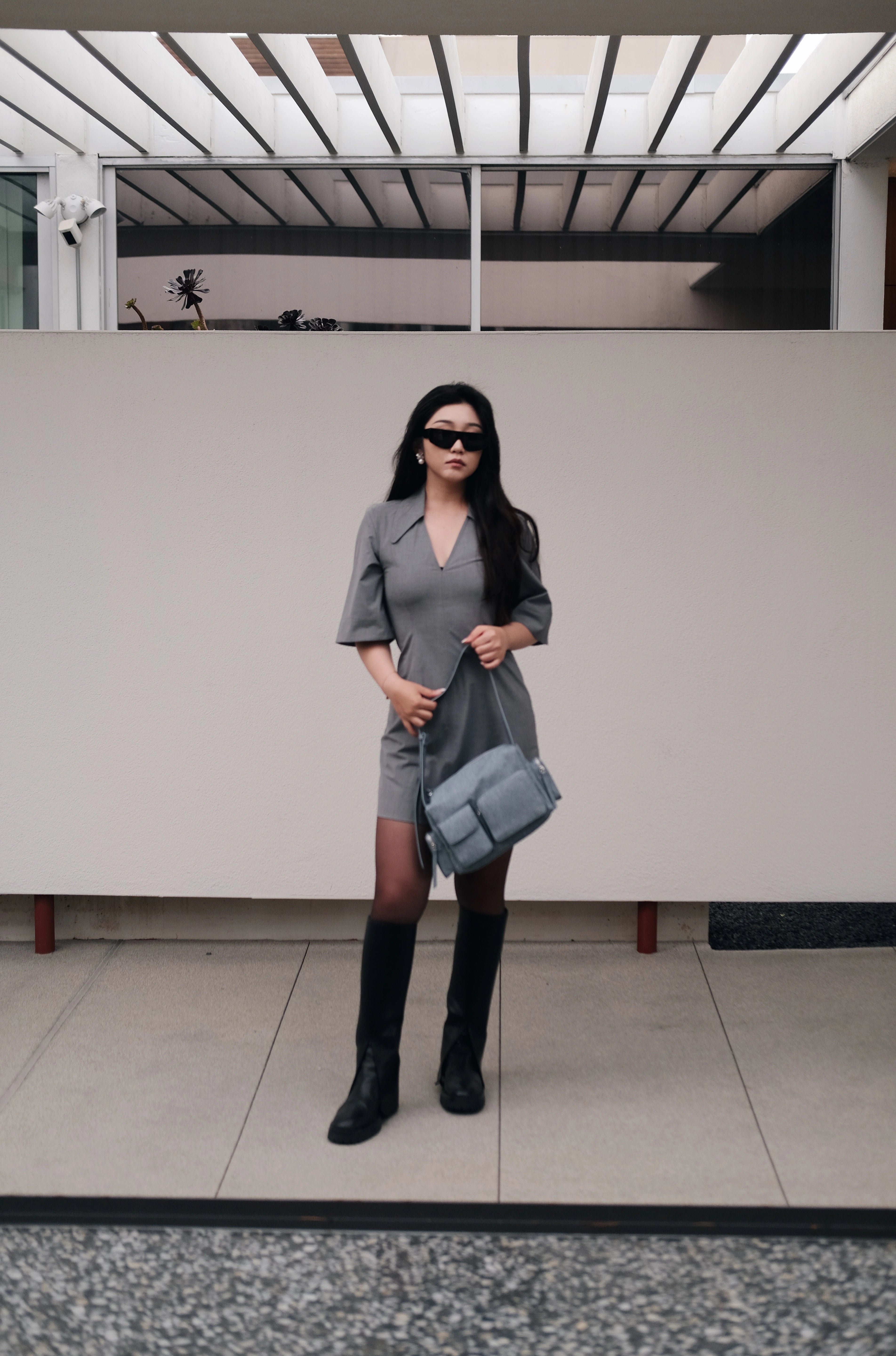 Model holding a blue large shoulder bag standing in front of a wall