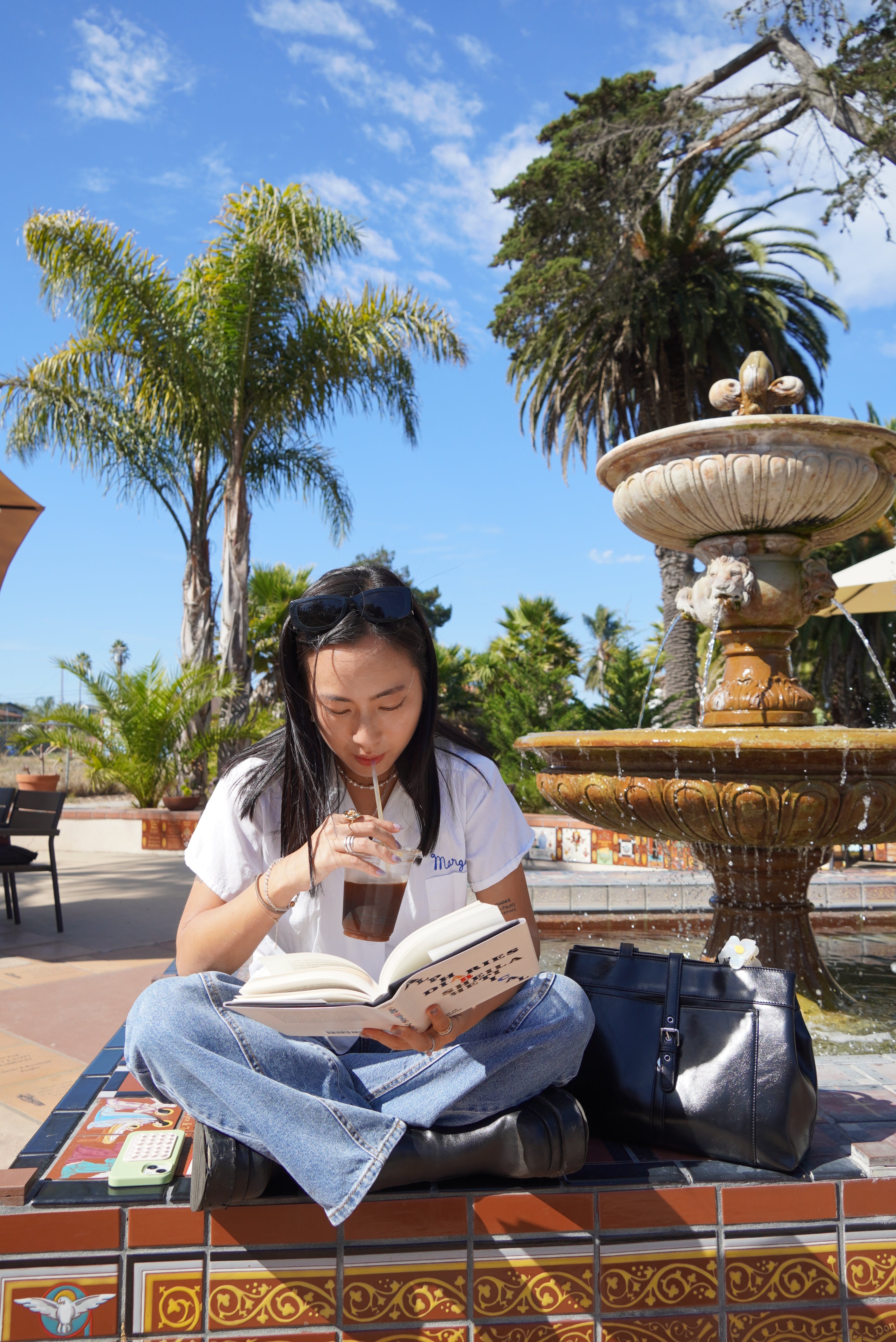 Girl reading a book while drinking coffee, with a black tote bag by her side.