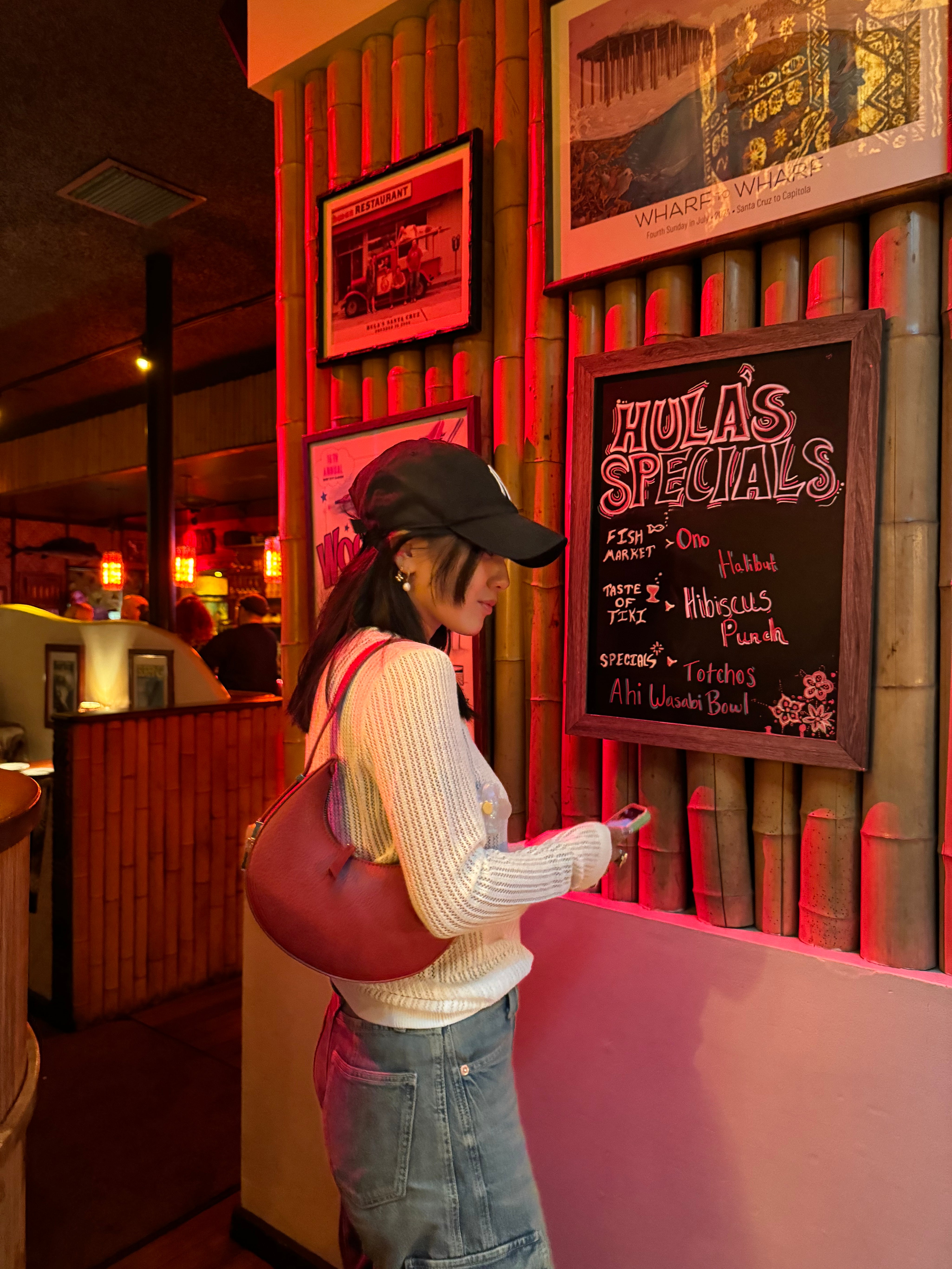 Girl holding a red mini crescent bag while standing in a bar.