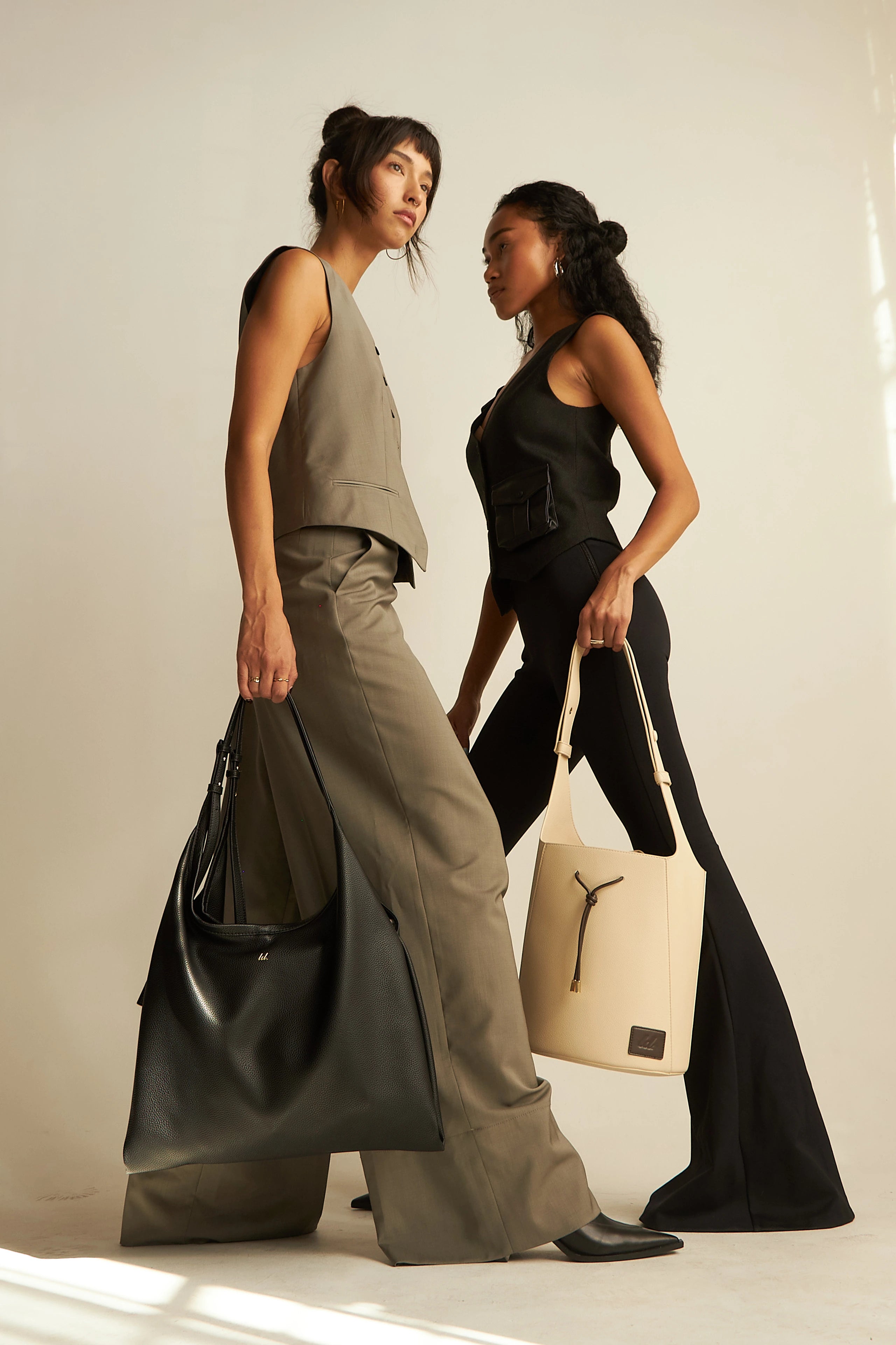 one model holding a black tote bag and the other holding a white bucket tote bag.