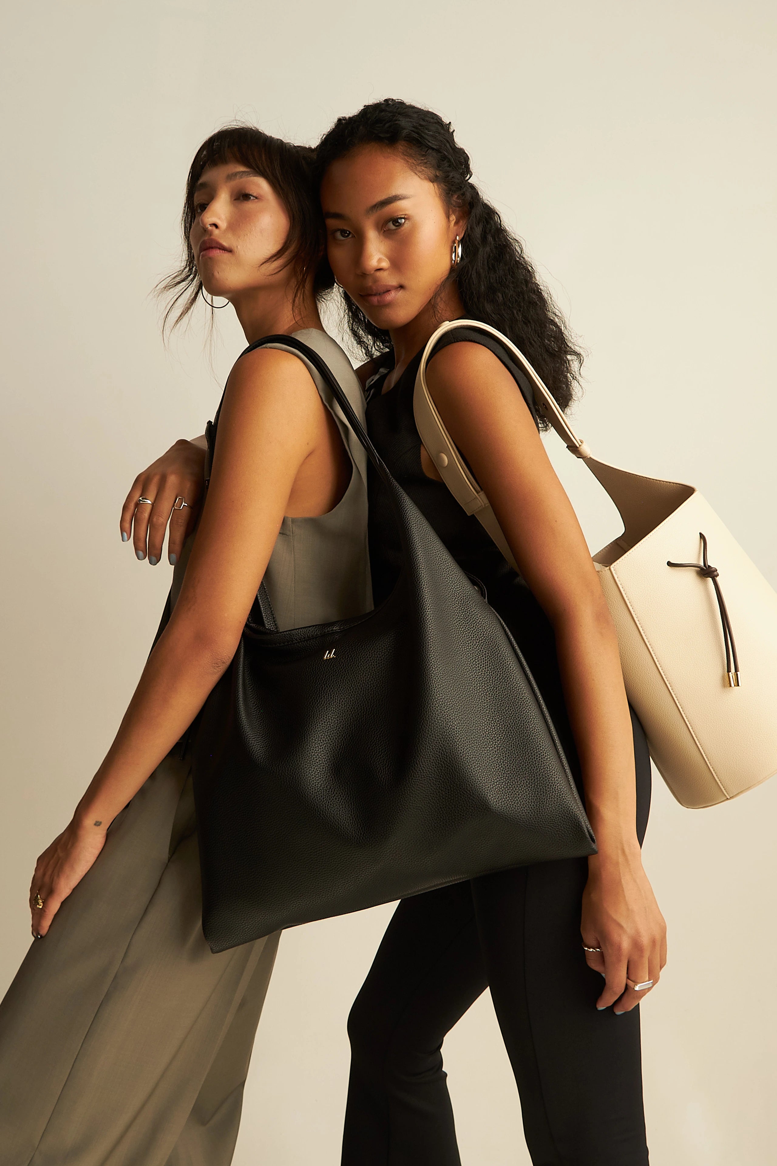 one model holding a black tote bag and the other holding a white bucket tote bag.