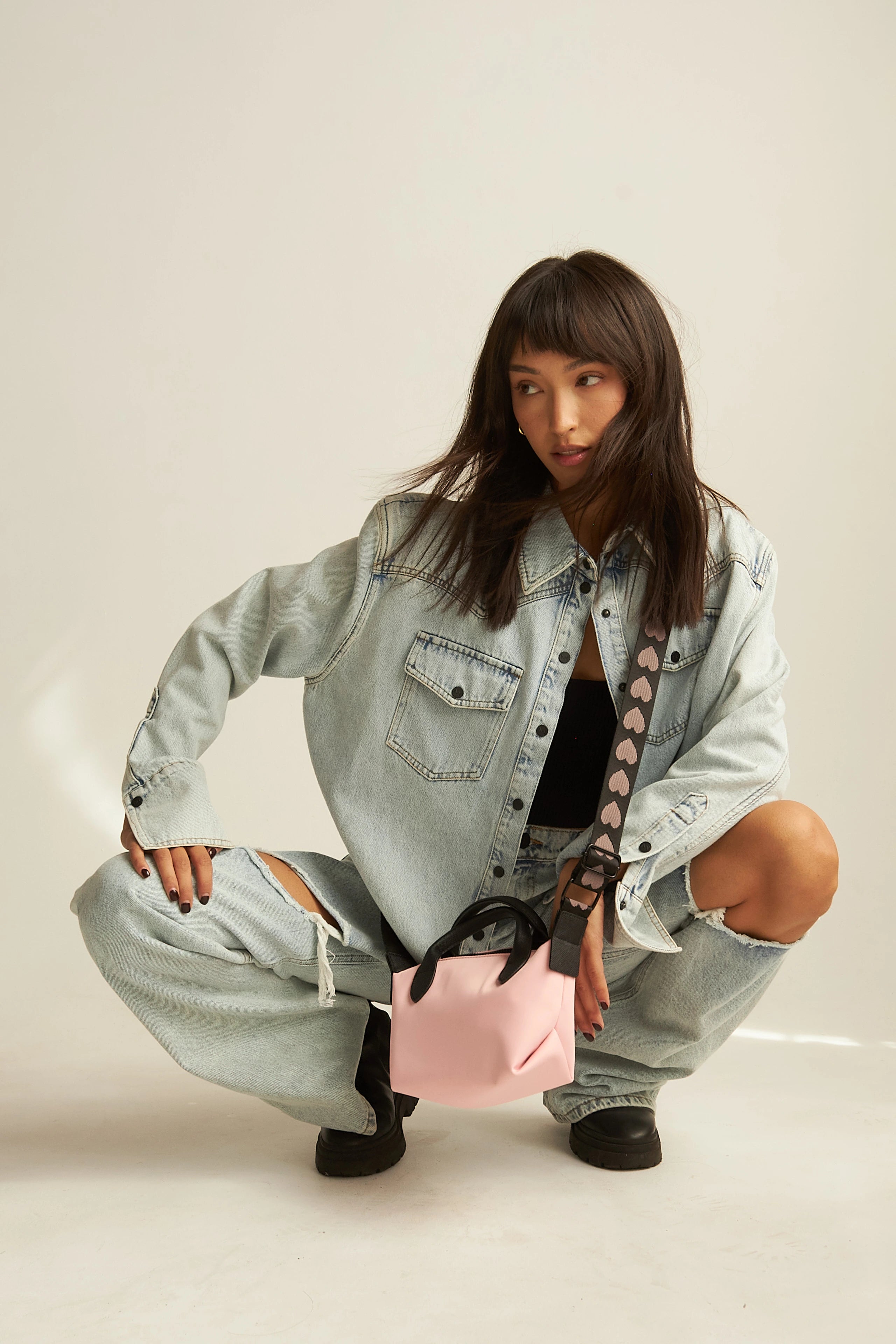 A model is holding a pink crossbody bag.