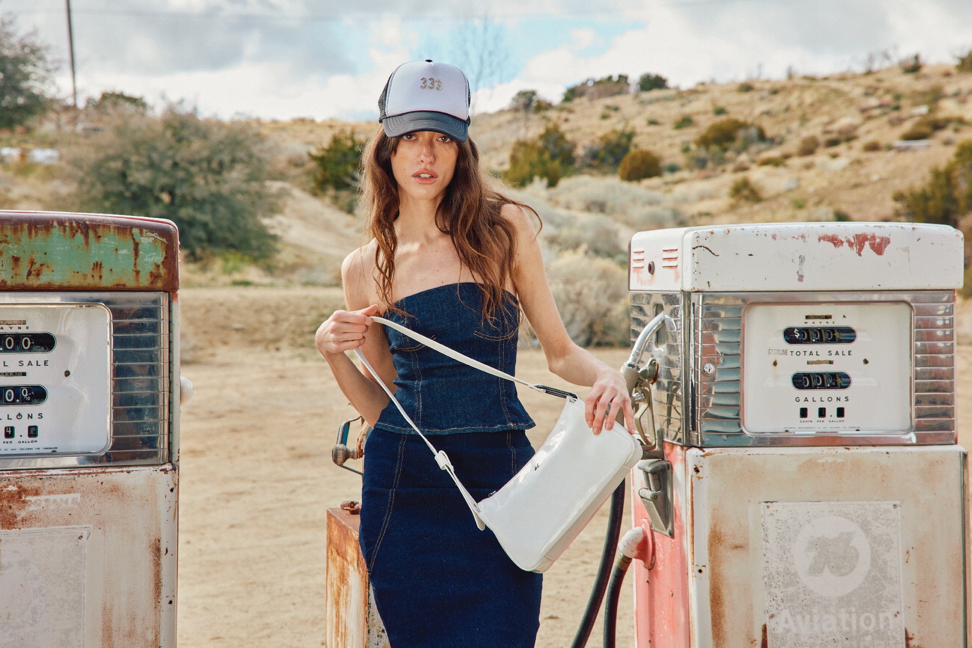 A model holding a white shoulder bag standing in the desert.