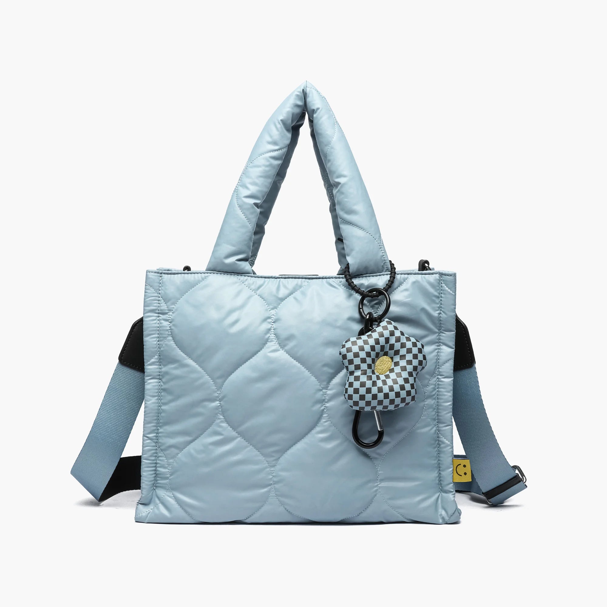 Blue quilted puffer tote bag with padded handles, checkered flower keychain, and adjustable shoulder strap