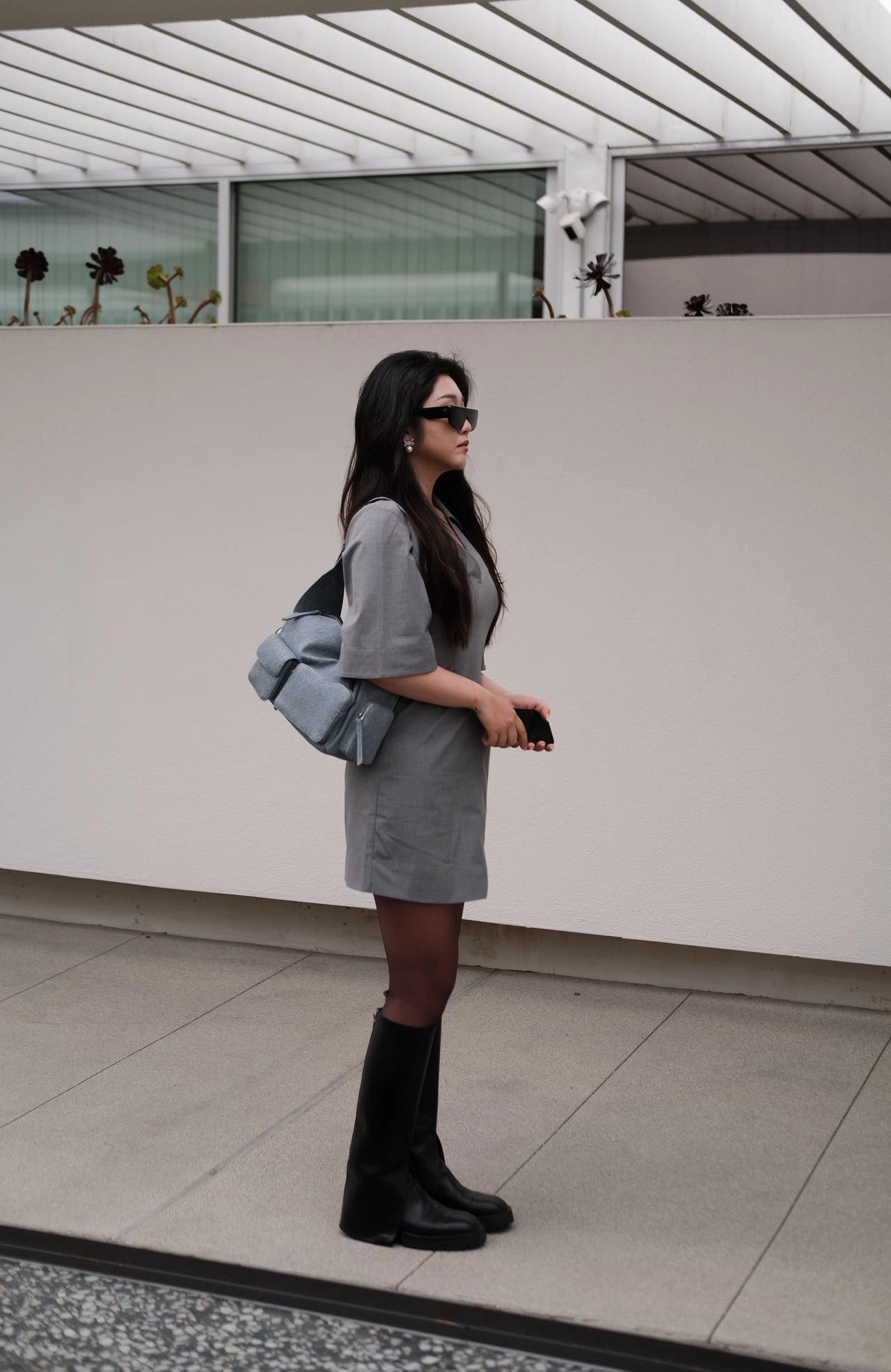 Model holding a blue large shoulder bag standing in front of a wall