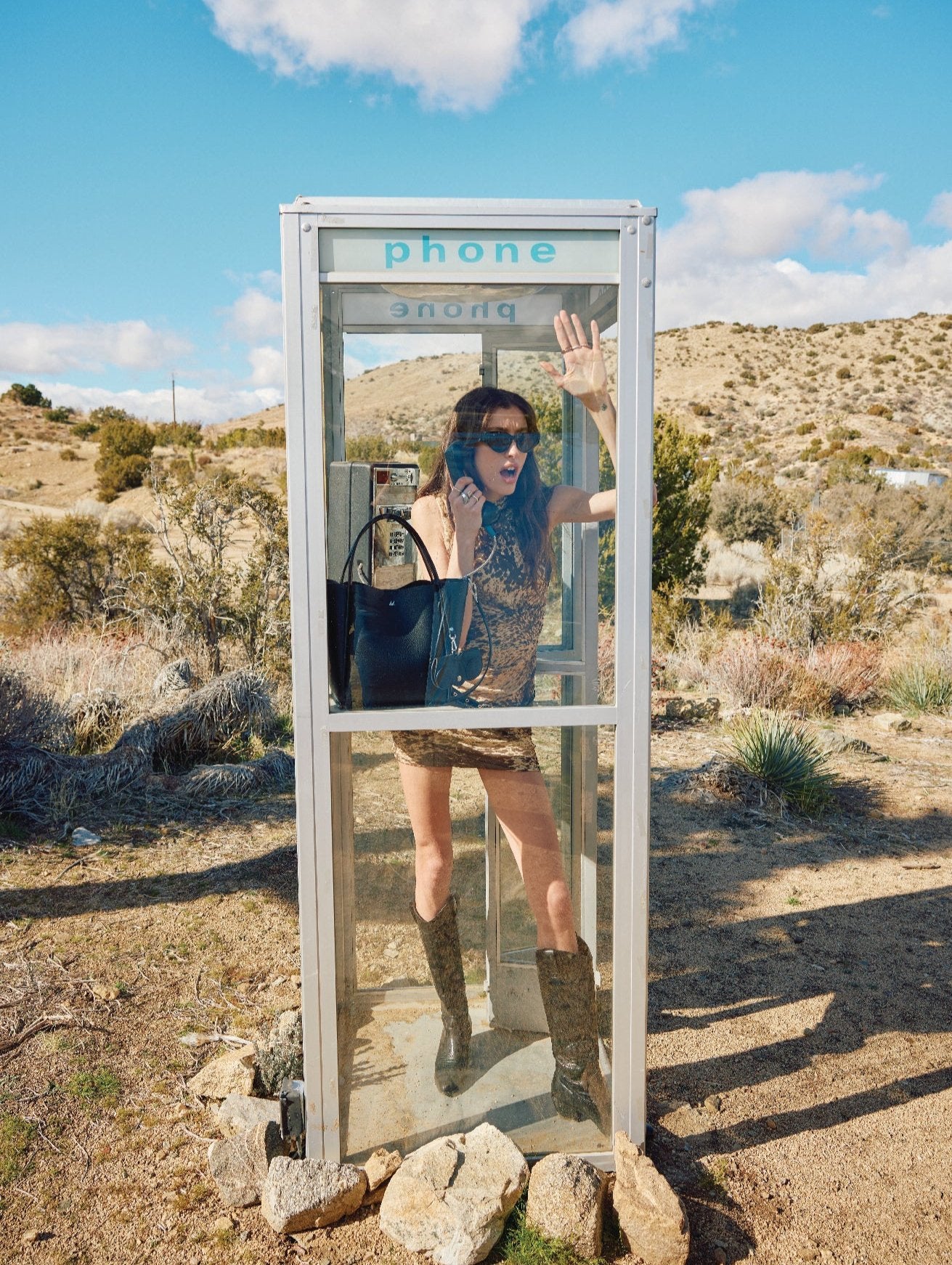 A girl standing in a phone booth holding a black tote bag.