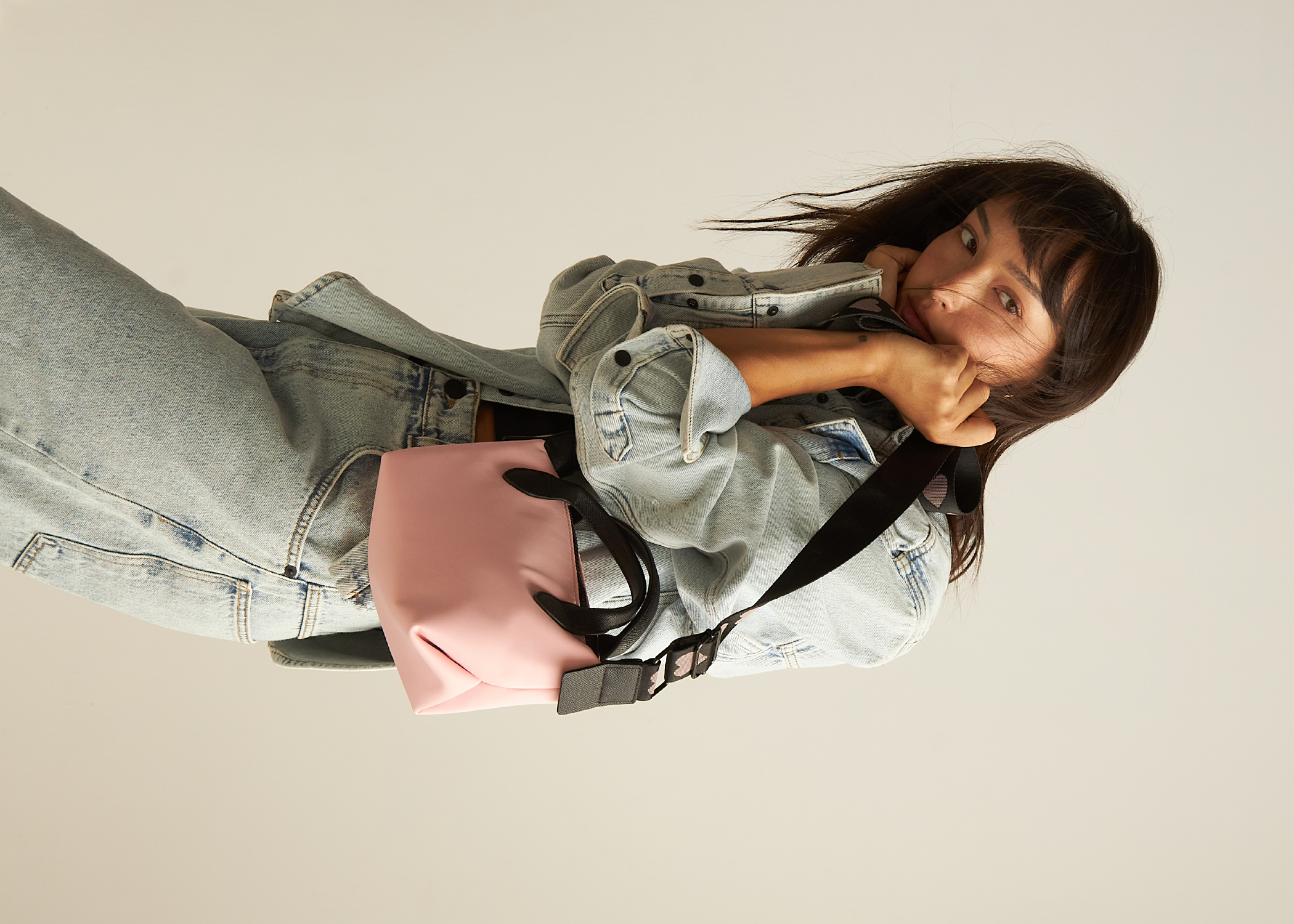 A model is holding a pink crossbody bag.